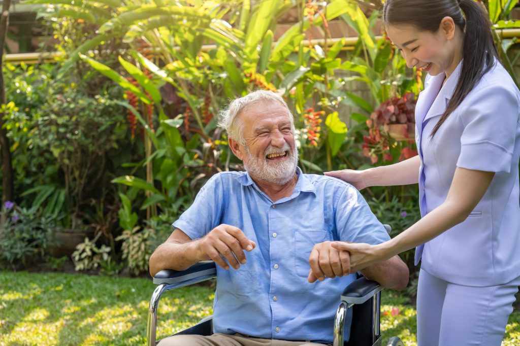 happy nurse holding laughing elderly man hand wheelchair garden nursing home